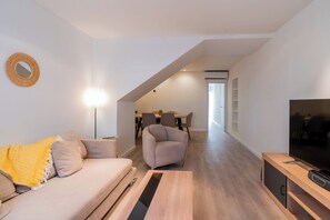 A modern living room with a sofa, a coffee table, a TV, and a dining area in the background.