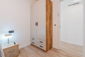 A bedroom with a wardrobe, bedside table, lamp, and a door with a vent.