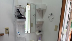 A bathroom with a white sink, mirror, and storage cabinets. There is a mop and bucket, and a power outlet on the wall.