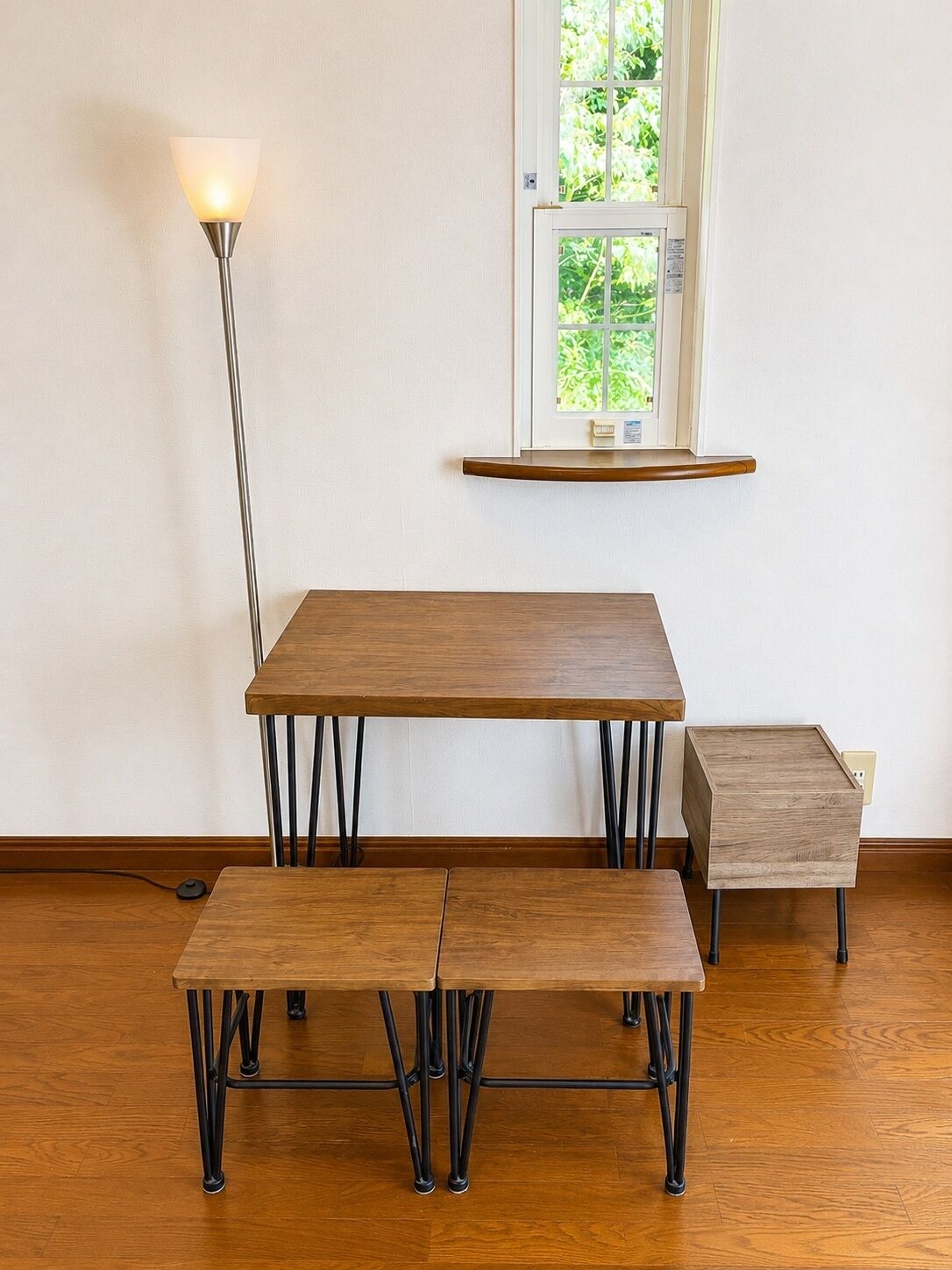 A dining area with a table and benches, a floor lamp, and a window with a view of greenery.
