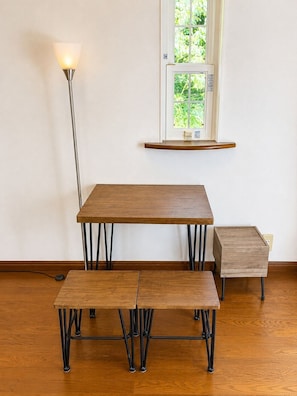 Un comedor con mesa y bancos, una lámpara de pie y un ventanal con vistas a la vegetación.
