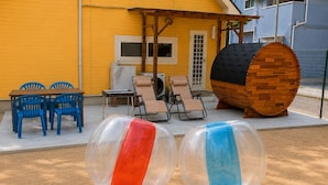 Two transparent inflatable balls, a wooden barrel, and outdoor furniture against a yellow building.