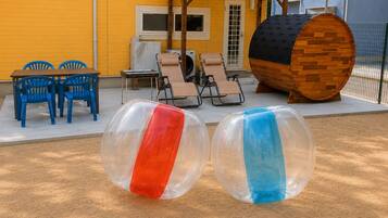 Two transparent inflatable balls, a wooden barrel, and outdoor furniture against a yellow building.