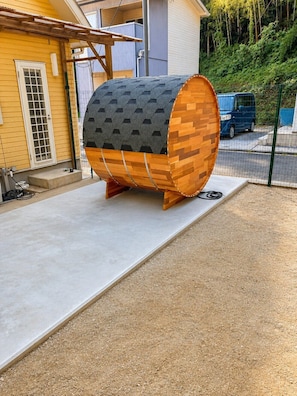 A cylindrical structure with a wooden exterior and a grey textured top, placed on a concrete surface in an outdoor setting.