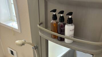 A bathroom with a bathtub, a shower, and a shelf with toiletries.