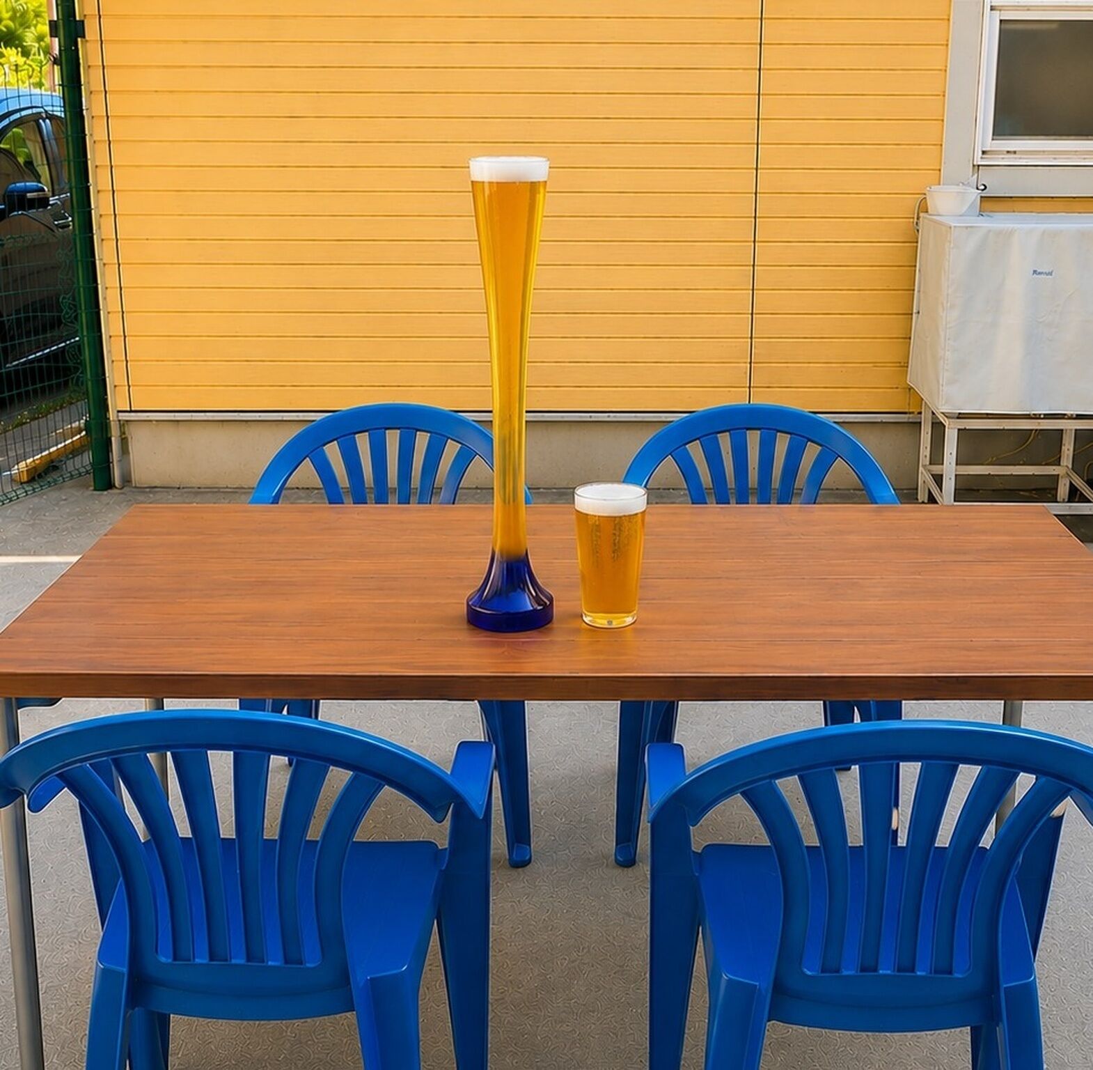 A wooden table with two blue chairs, a tall glass, and a shorter glass of beer.