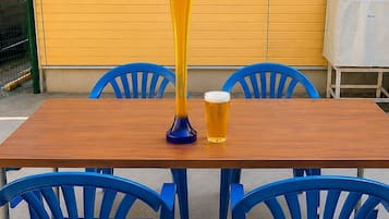 A wooden table with two blue chairs, a tall glass, and a shorter glass of beer.