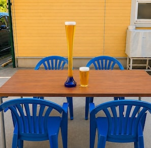 A wooden table with two blue chairs, a tall glass, and a shorter glass of beer.