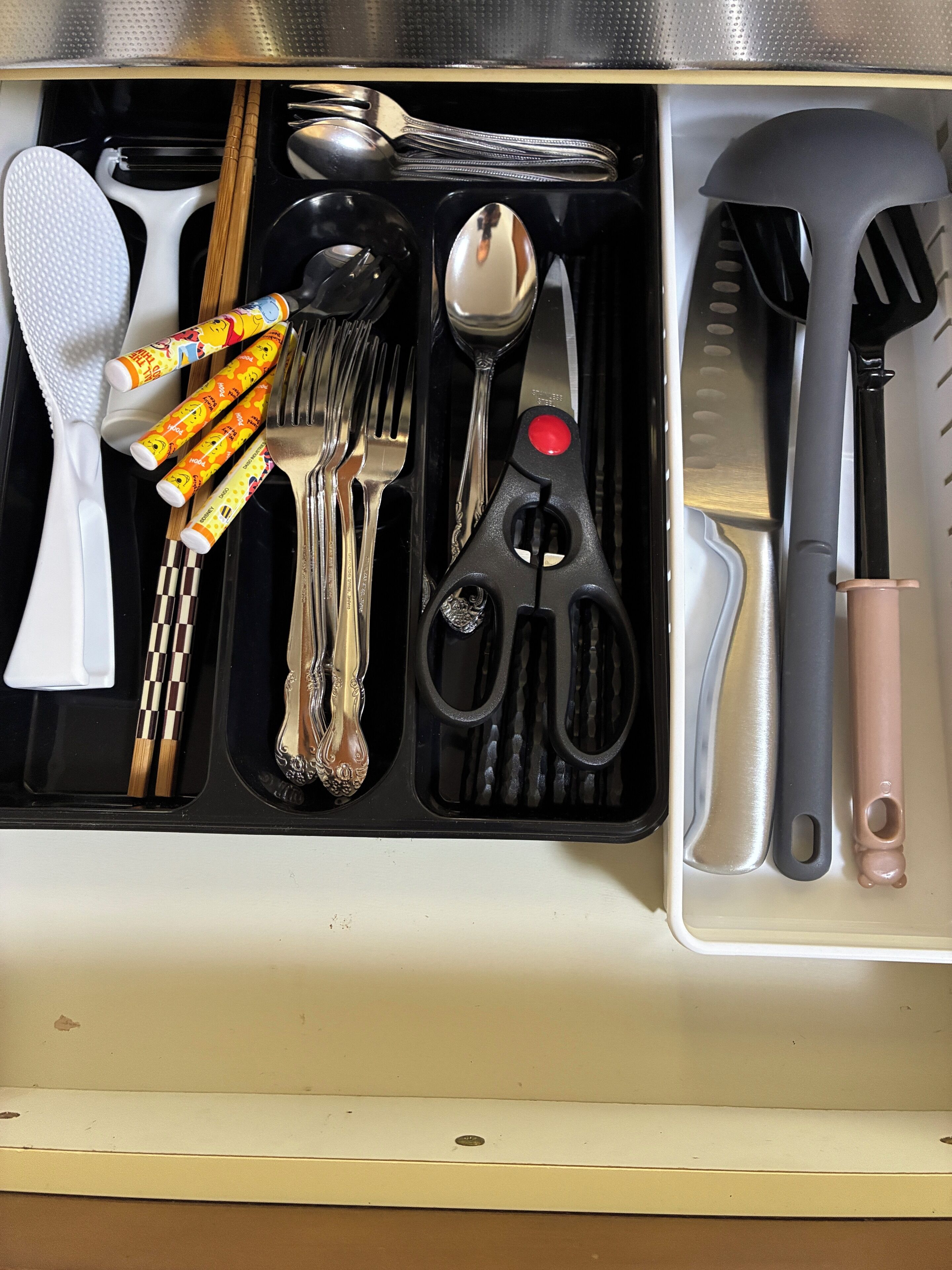 A drawer with various utensils including forks, spoons, and a pair of scissors.