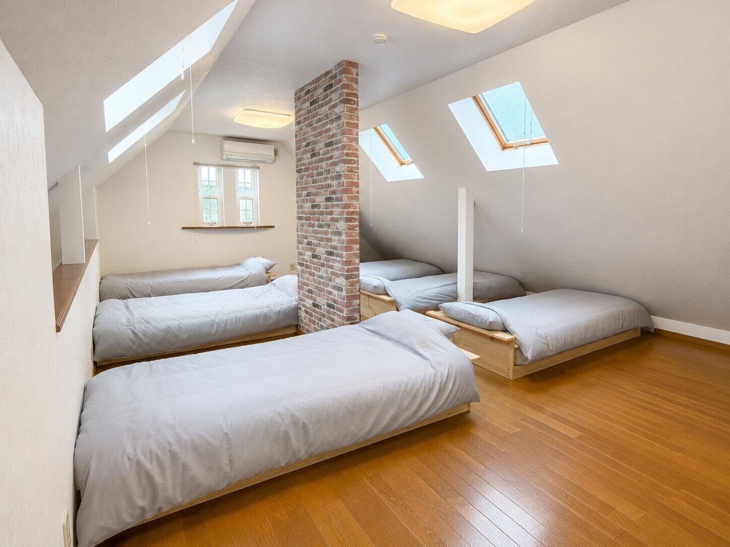 A dormitory-style room with three bunk beds, skylights, and a brick accent wall.