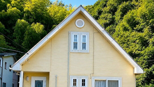 A two-story building with a gabled roof, a front door, and two air conditioning units on the ground floor.