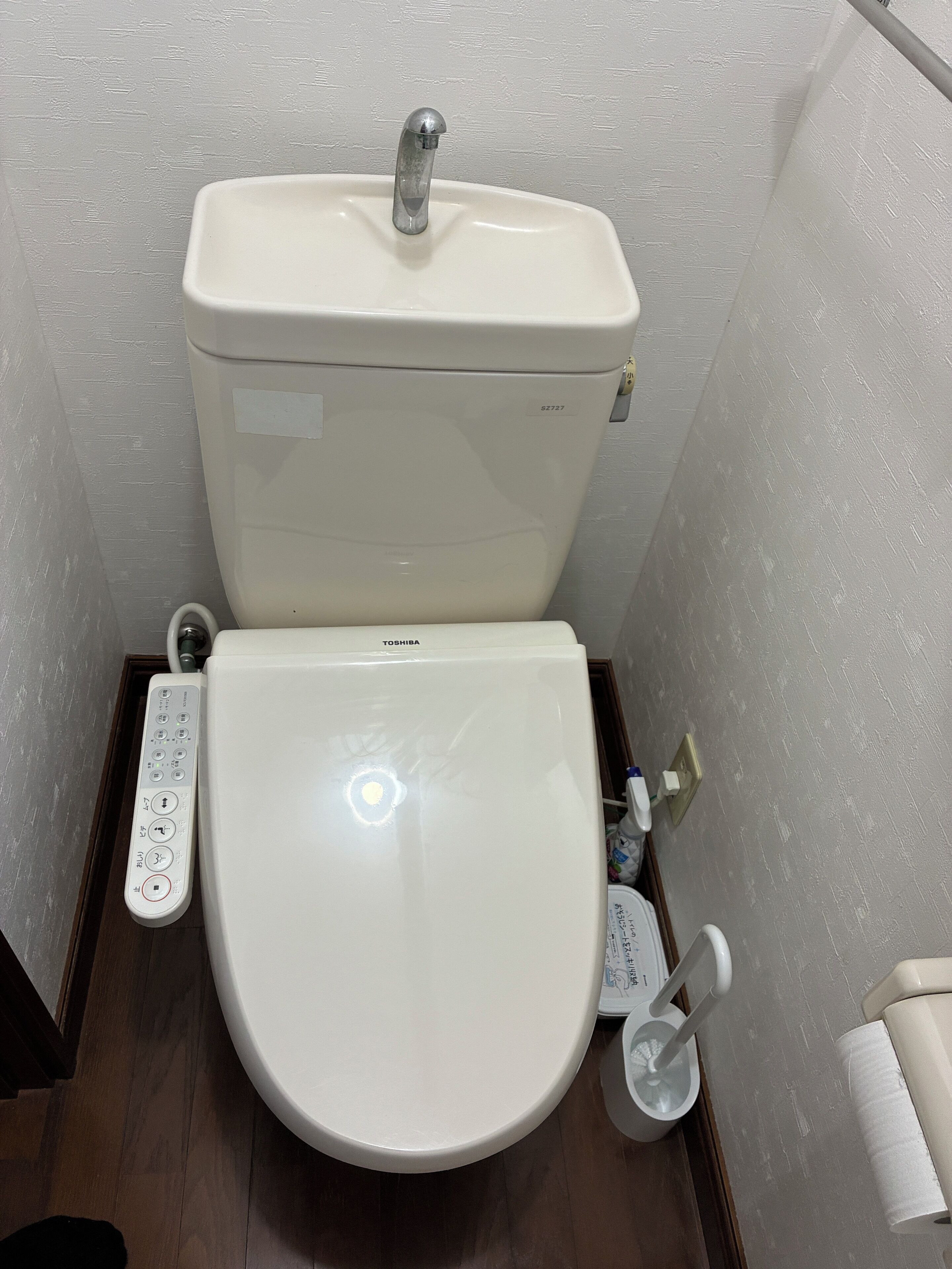 Toilet met bedieningspaneel, toiletrolhouder en een douchetoilet.