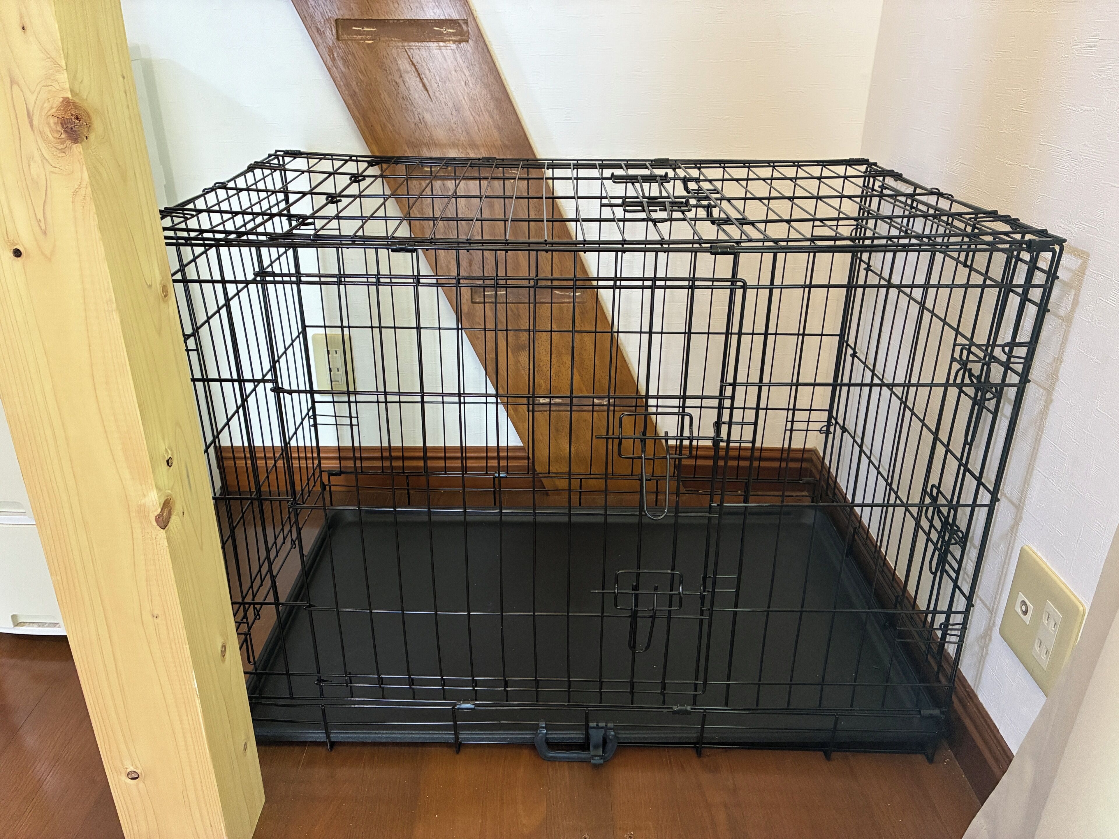 Una jaula de metal negro con suelo de madera, ubicada junto a una pared con una viga de madera.