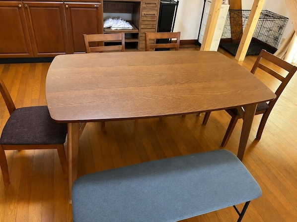 A wooden dining table with four chairs, a bench, and a cabinet with a shelf.