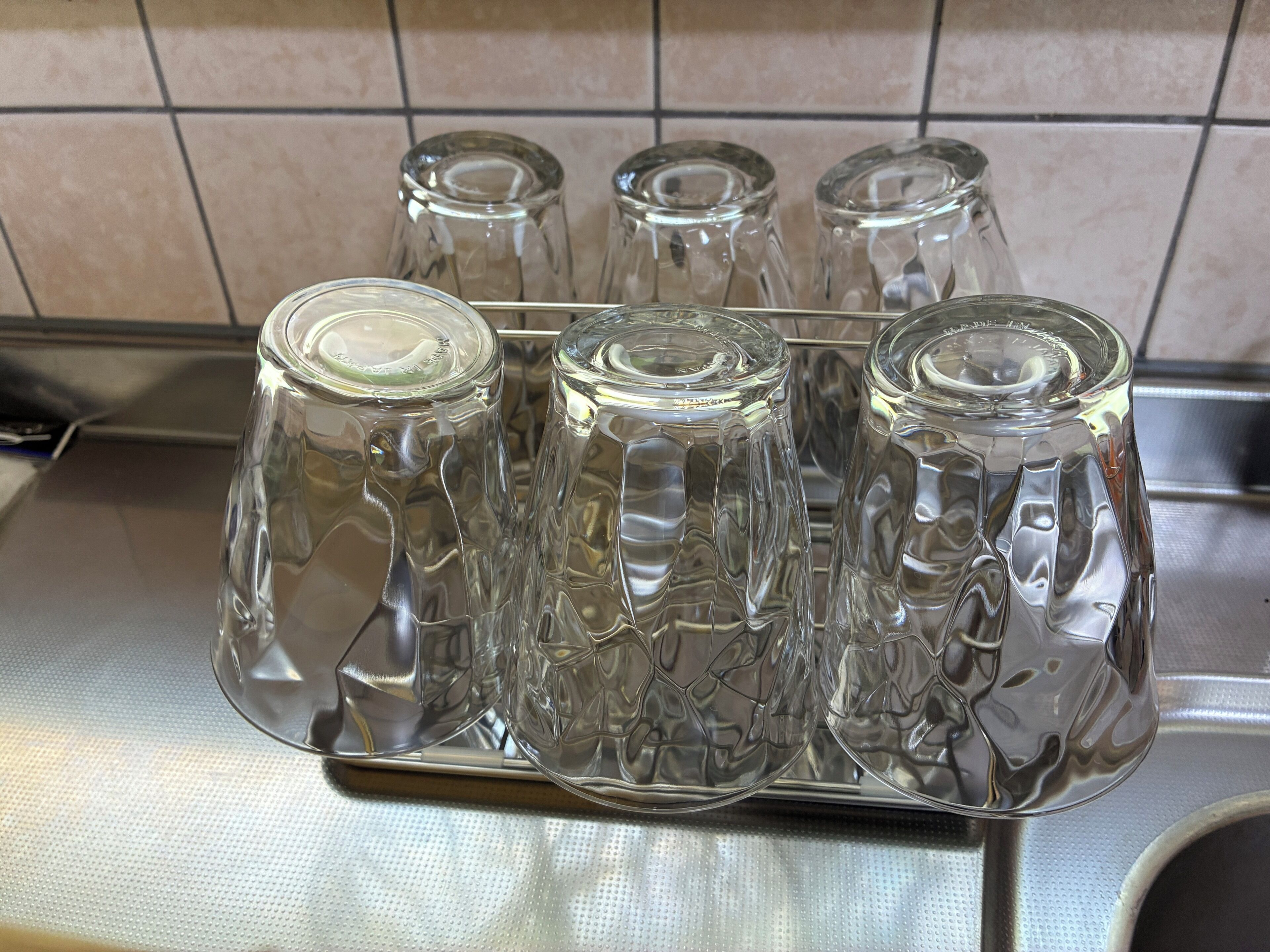 A stainless steel rack holding four clear glass tumblers with embossed patterns.