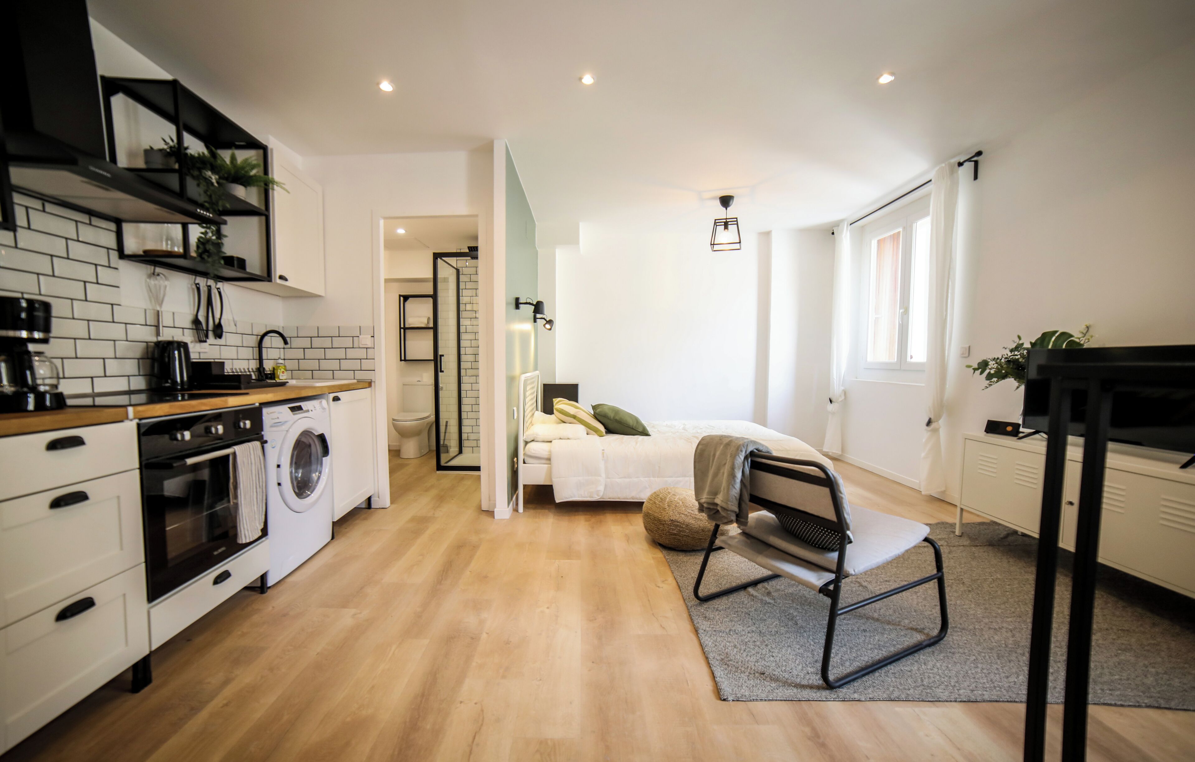 A compact living space with a kitchenette, a bed, a seating area, and a bathroom.
