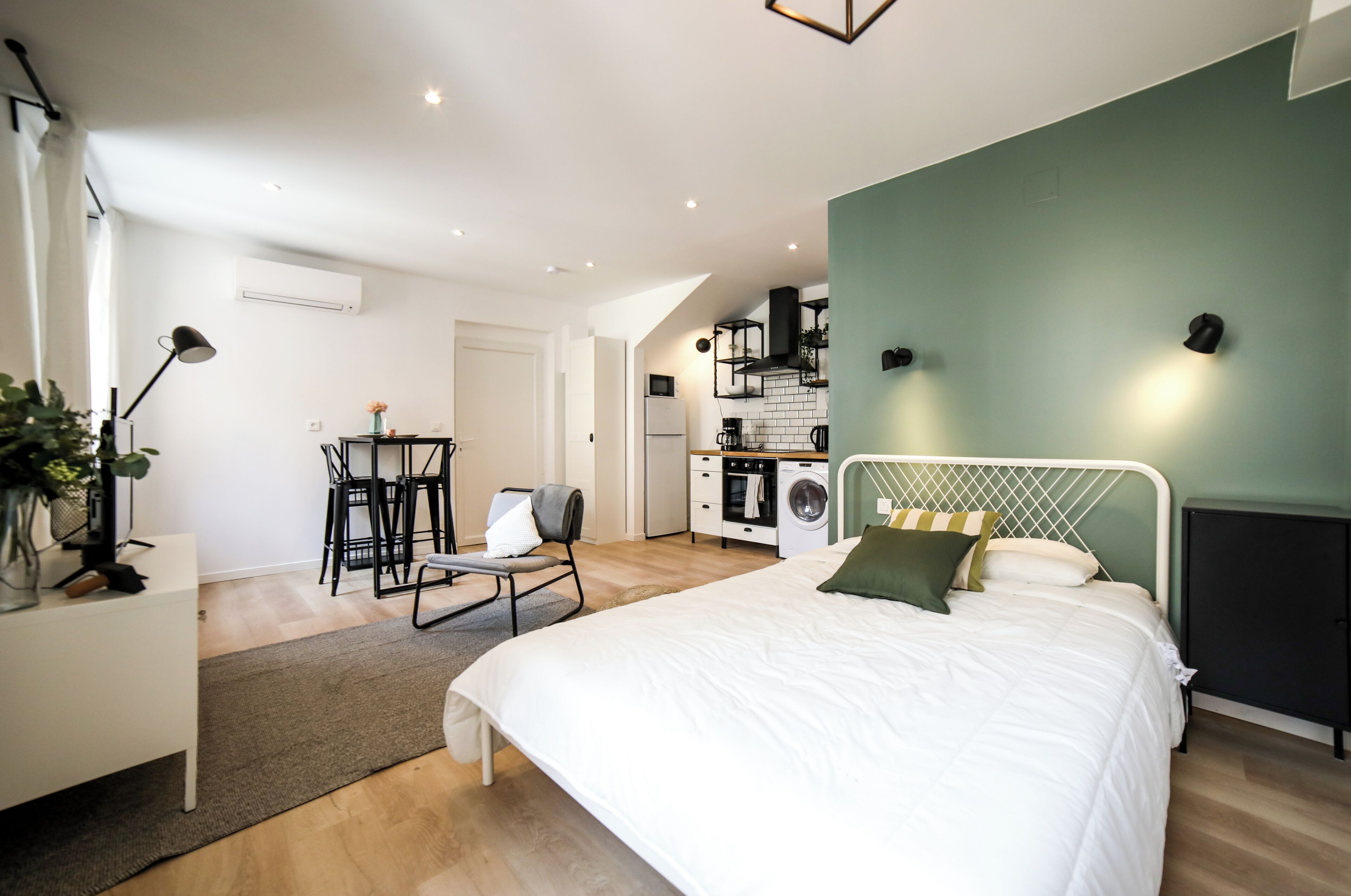 A modern bedroom with a large bed, a desk, and a kitchenette.