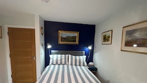 A bedroom with a bed, two bedside lamps, a door, and two framed pictures on the wall.
