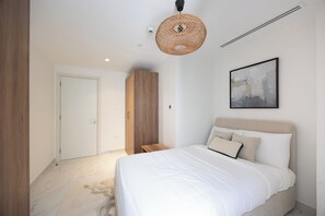 Une chambre à coucher comprenant un lit, une armoire, une porte, un luminaire suspendu et un tableau encadré accroché au mur.