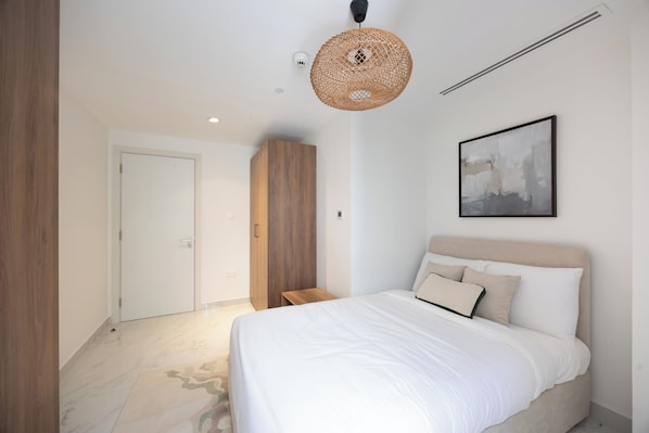 A bedroom with a bed, a wardrobe, a door, a hanging light fixture, and a framed picture on the wall.
