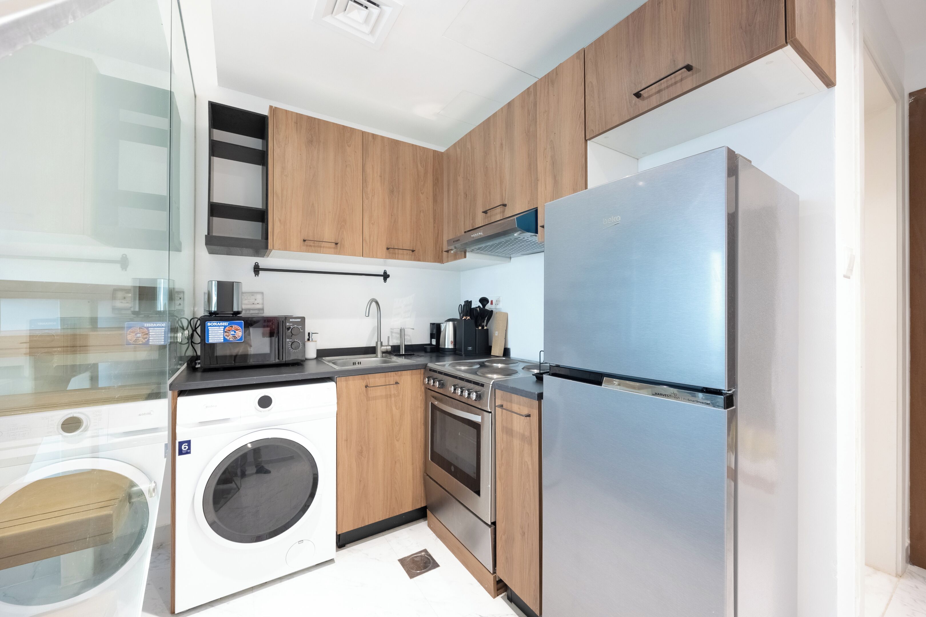 A modern kitchen with wooden cabinets, a stainless steel refrigerator, a built-in washing machine, and a gas stove.