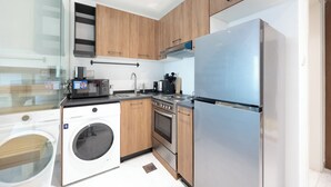 A modern kitchen with wooden cabinets, a stainless steel refrigerator, a built-in washing machine, and a gas stove. - Bloomfields 2br Duplex in Oasis 1  (Abu Dhabi)