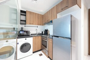 Eine moderne Küche mit Holzschränken, einem Edelstahlkühlschrank, einer integrierten Waschmaschine und einem Gasherd.