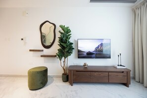 Un salon moderne avec un téléviseur à écran plat, un miroir, une plante en pot, un pouf vert et une console en bois.