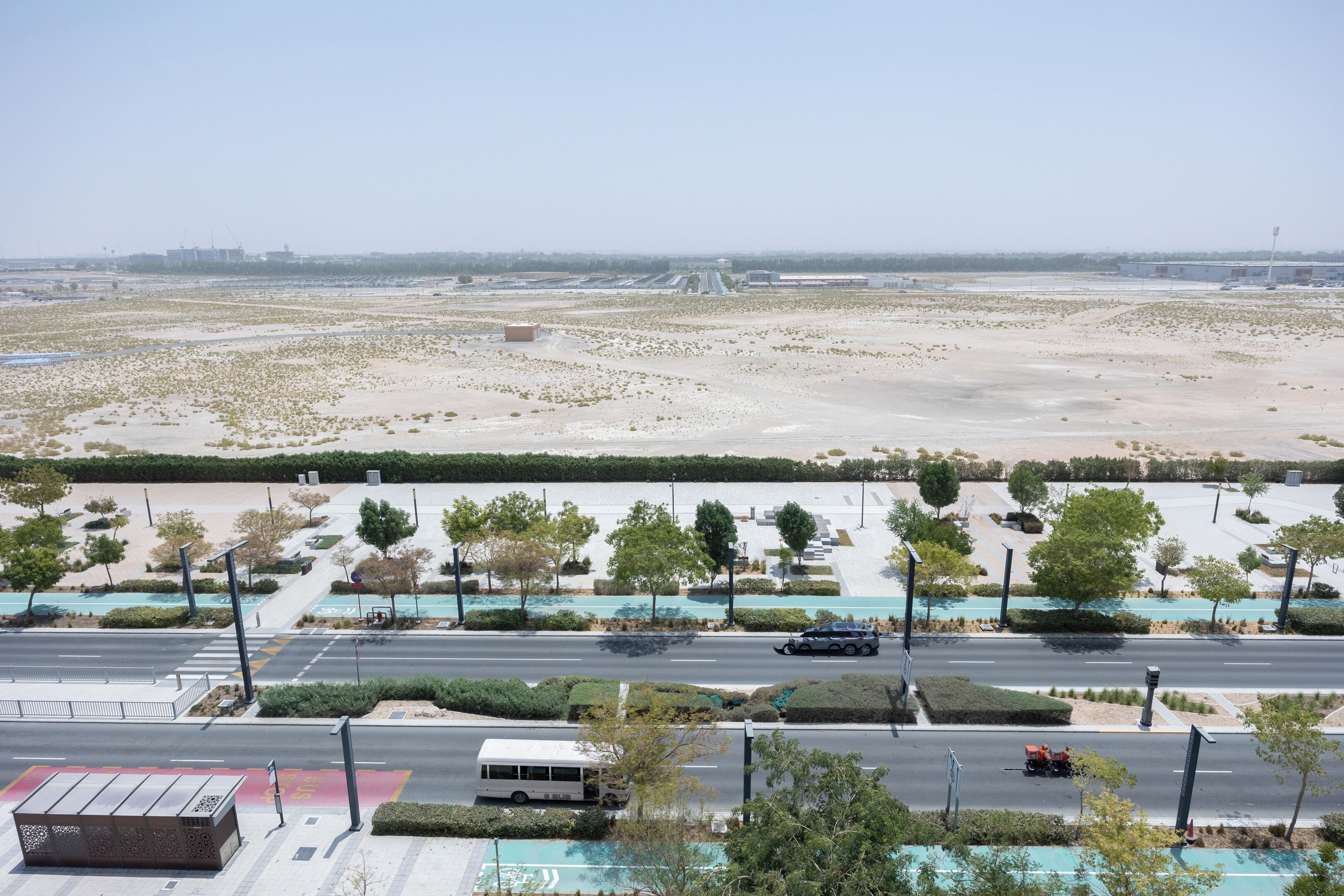 A parking lot with a bus and a truck, surrounded by greenery and buildings.
