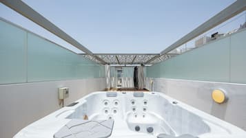 A modern outdoor hot tub with a glass enclosure, a control panel, and a seating area.
