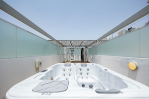 A modern outdoor hot tub with a glass enclosure, a control panel, and a seating area.