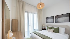 A hotel room with a bed, a desk, a chair, a lamp, and two paintings on the wall. - Bloomfields 2br Duplex in Oasis 1  (Abu Dhabi)