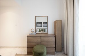 Quarto minimalista com cômoda de madeira, um espelho e um banquinho verde.