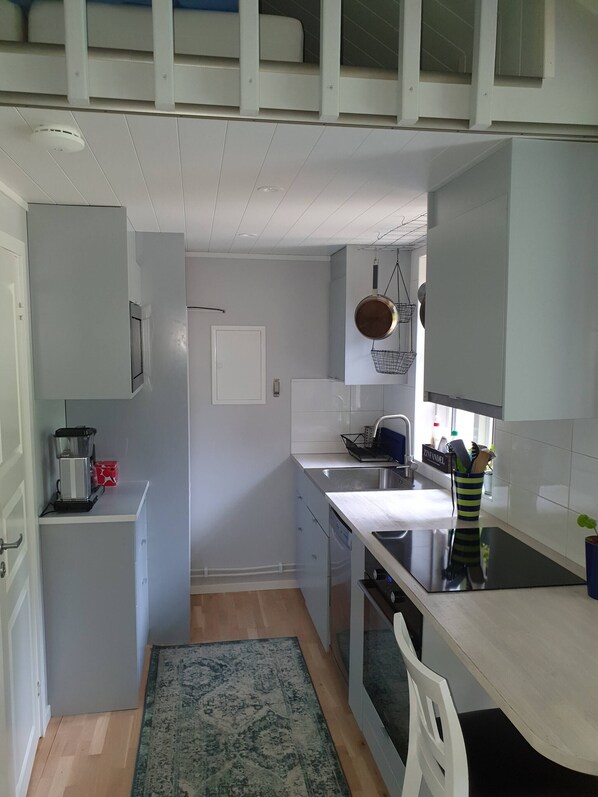 A compact kitchen with a built-in oven, a sink, and a stove. There is a small refrigerator and a coffee maker on the counter.