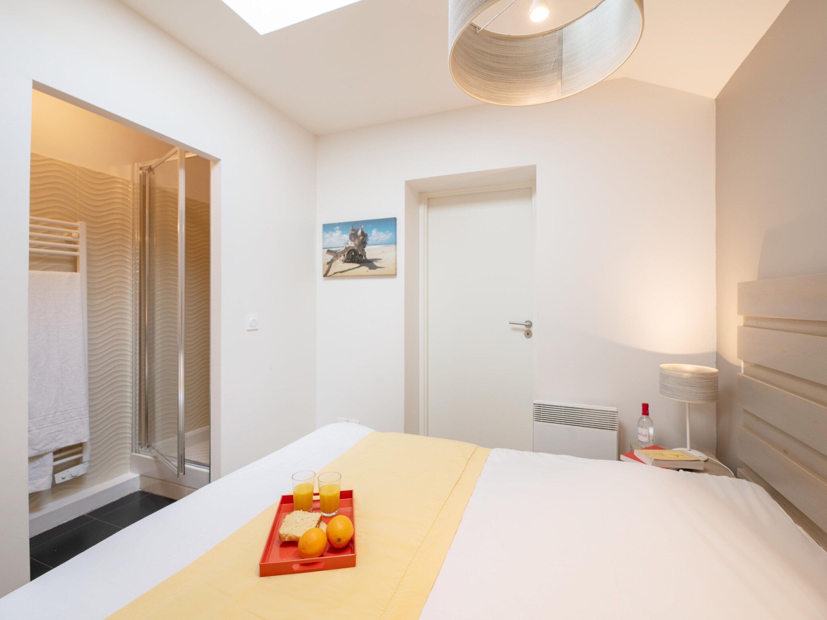 A hotel room with a bed, a breakfast tray with orange juice and bread, a painting on the wall, and a skylight.