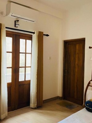 Une pièce avec une porte en bois, une fenêtre avec des rideaux, un radiateur et un petit paillasson à l’entrée.
