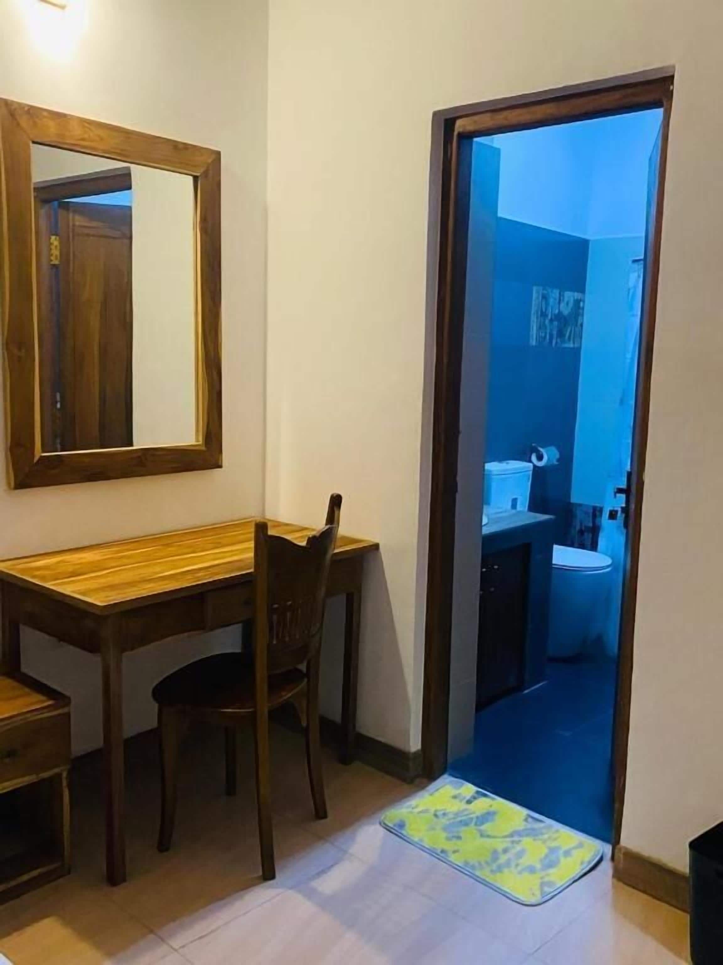 A room with a wooden desk, a chair, a mirror, and a door leading to a bathroom.