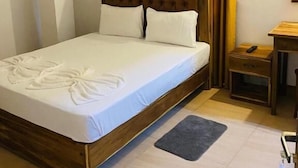 A hotel room with a wooden bed, a bedside table, a small nightstand, and a window with curtains.