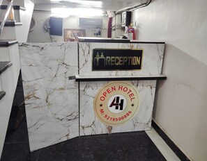 Ein Empfangsbereich mit einer Marmordesign-Theke, einem Schild mit der Aufschrift 'RECEPTION' und einem runden Schild mit 'HOTEL GEÖFFNET' und einer Telefonnummer.