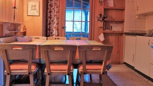 En matplats med ett träbord och stolar, ett fönster med gardiner och ett köksområde med skåp och en mikrovågsugn.