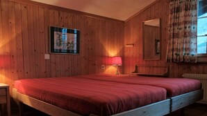 Ett rum med träpanel på väggarna, en säng, ett nattduksbord, en lampa och ett fönster med gardiner.