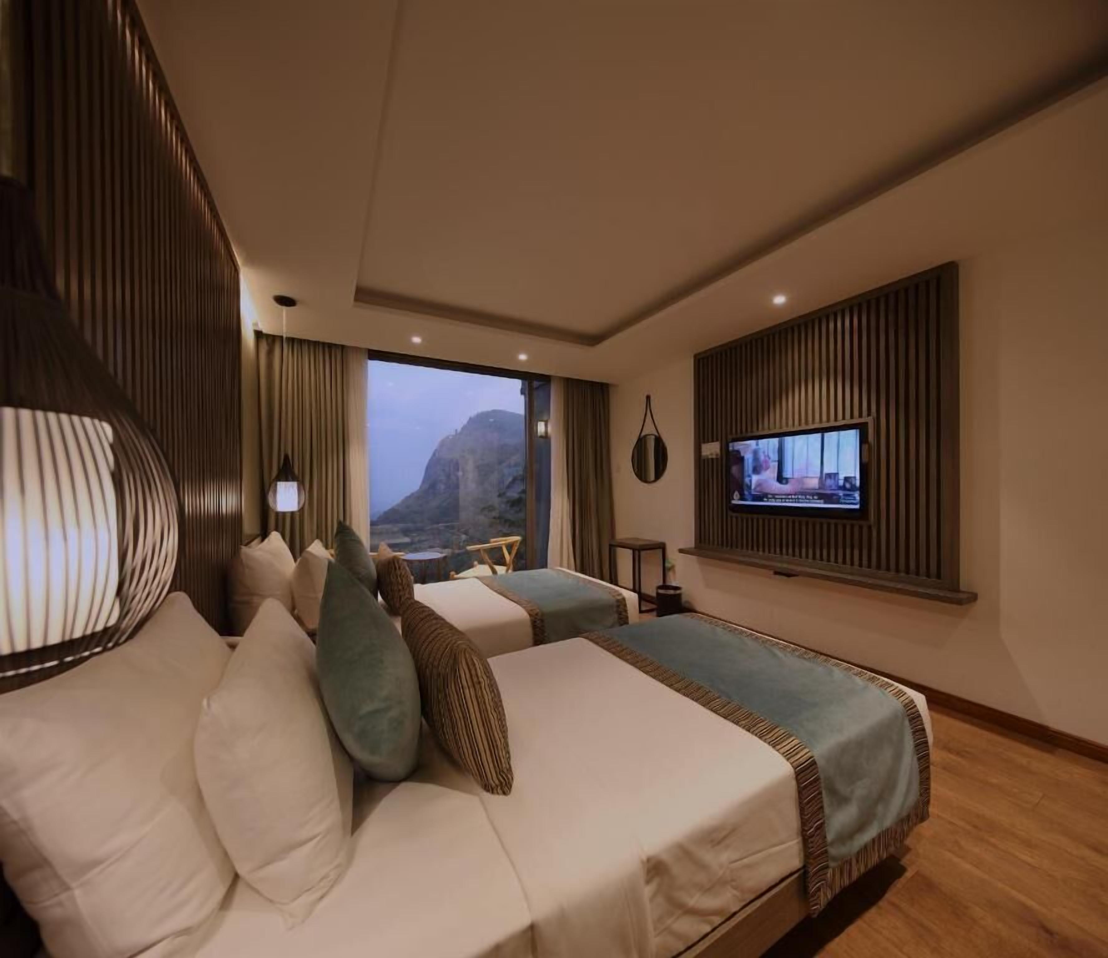 A hotel room with a bed, a TV, and a view of the mountains.