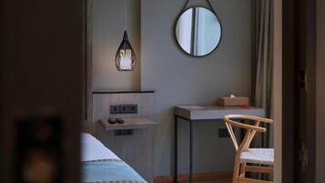 Ett hotellrum med en säng, ett skrivbord, en stol, en spegel och en hängande lampa.