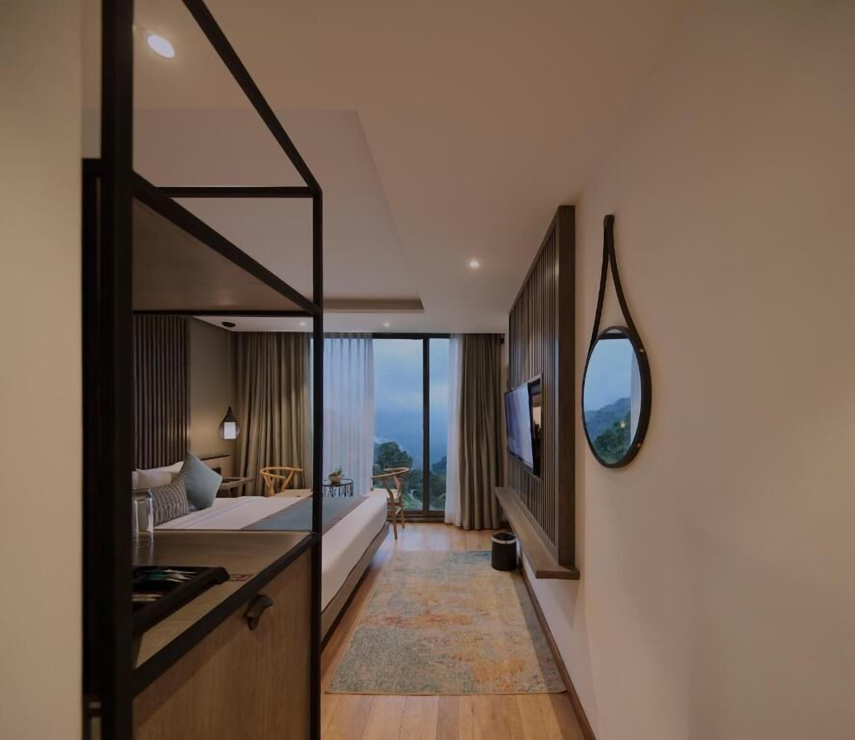 A hotel room with a bed, a desk, a chair, a TV, and a large window offering a view.