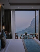 Habitación de hotel con una cama grande, una mesita, dos sillas y vistas a la montaña.