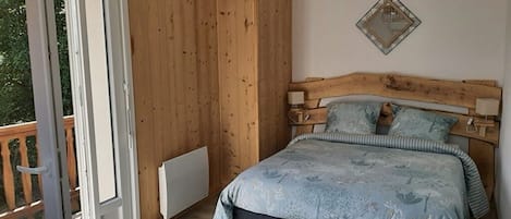 Et soveværelse med sengegavl i træ, seng med blomstret dynebetræk, et natbord og et spejl monteret på væggen.
