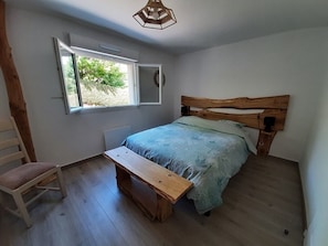 A bedroom with a wooden headboard, a single bed, a bench, a chair, and a window with a view of greenery. - A 3-star vacation home with great amenities. (Le Tholy)