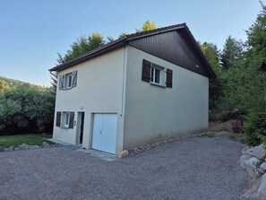A two-story building with a garage, surrounded by a gravel driveway and greenery. - Renovated house near Gérardmer (Le Tholy)