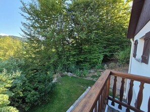 A balcony with a wooden railing overlooking a lush green garden and dense forest. - A 3-star vacation home with great amenities. (Le Tholy)