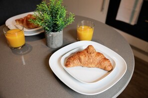 A breakfast setting with a croissant on a plate, two glasses of orange juice, and a small potted plant.